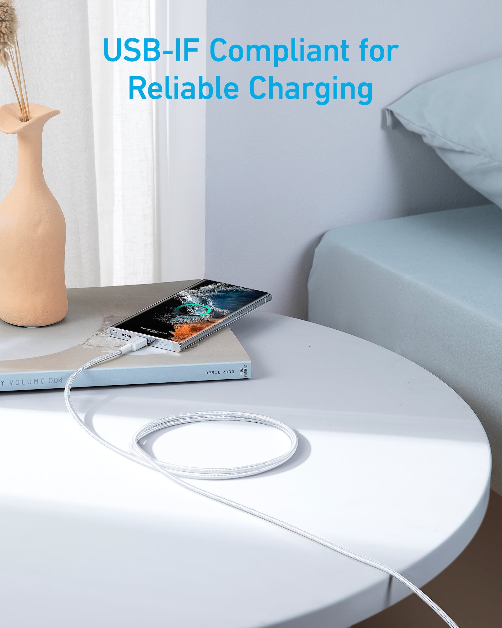 Smartphone with charging cable on a table in a modern living room setting, featuring USB-IF compliance text.