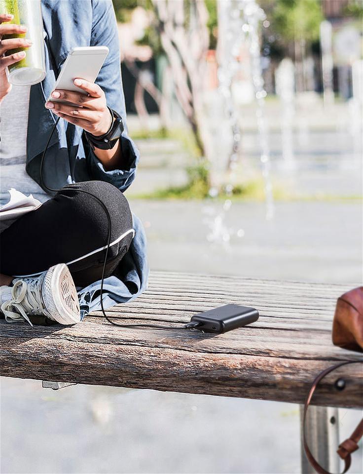 Portable power bank charging phone on park bench, Anker Kuwait